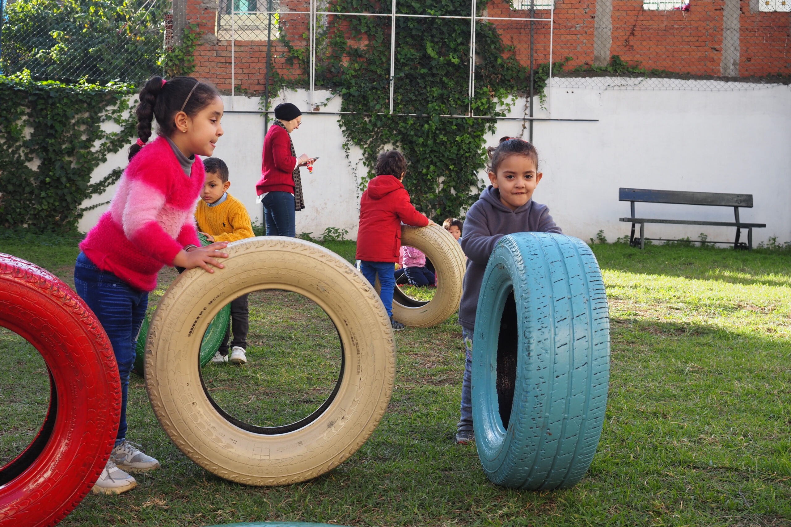Children playing outside with car tyres coloured pink and light blue